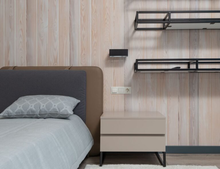 Neatly organised small wooden nightstand with bedside tray holding phone and glasses in cozy bedroom