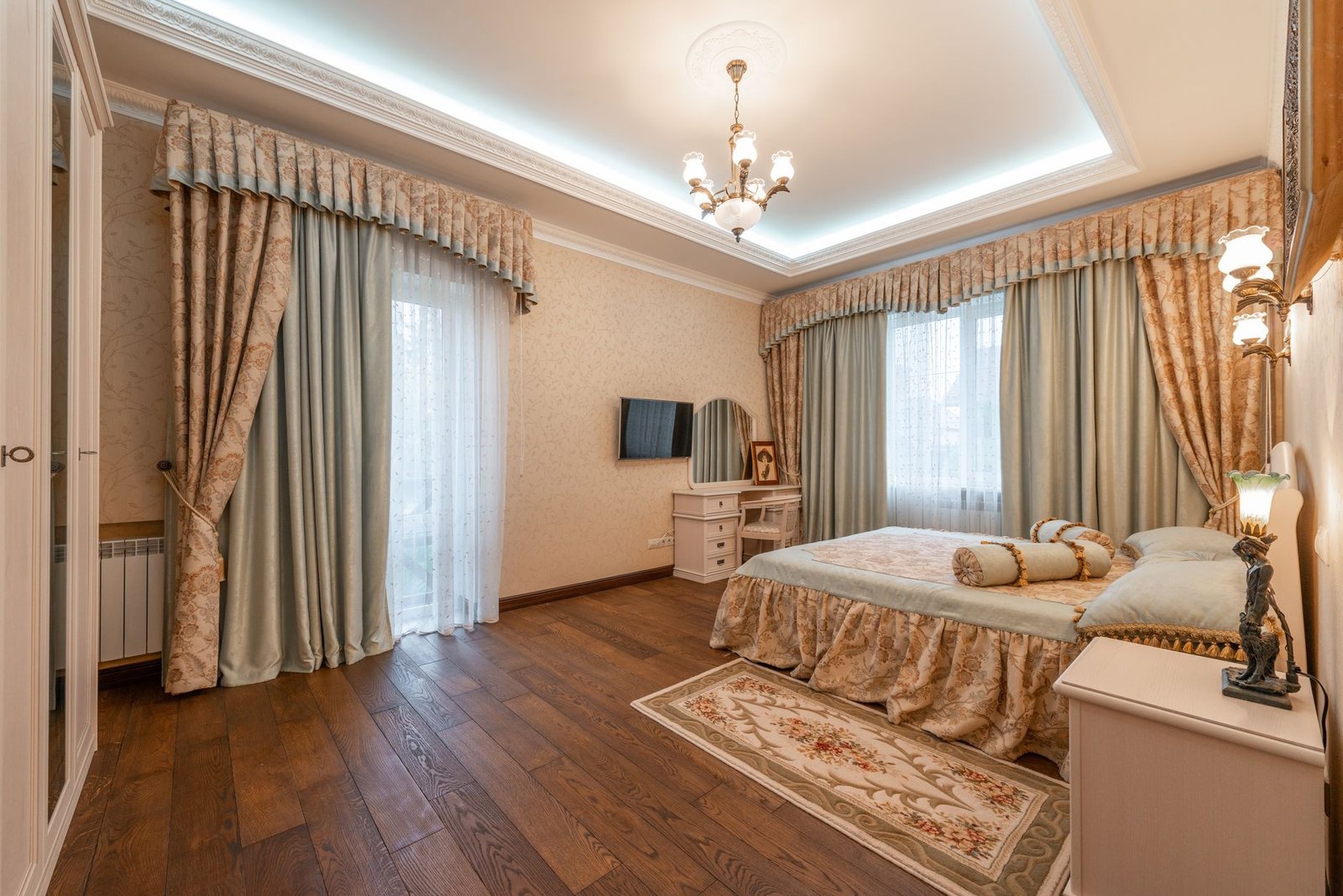 Cozy bedroom with layered area rug on hardwood floor next to white bedding and natural light