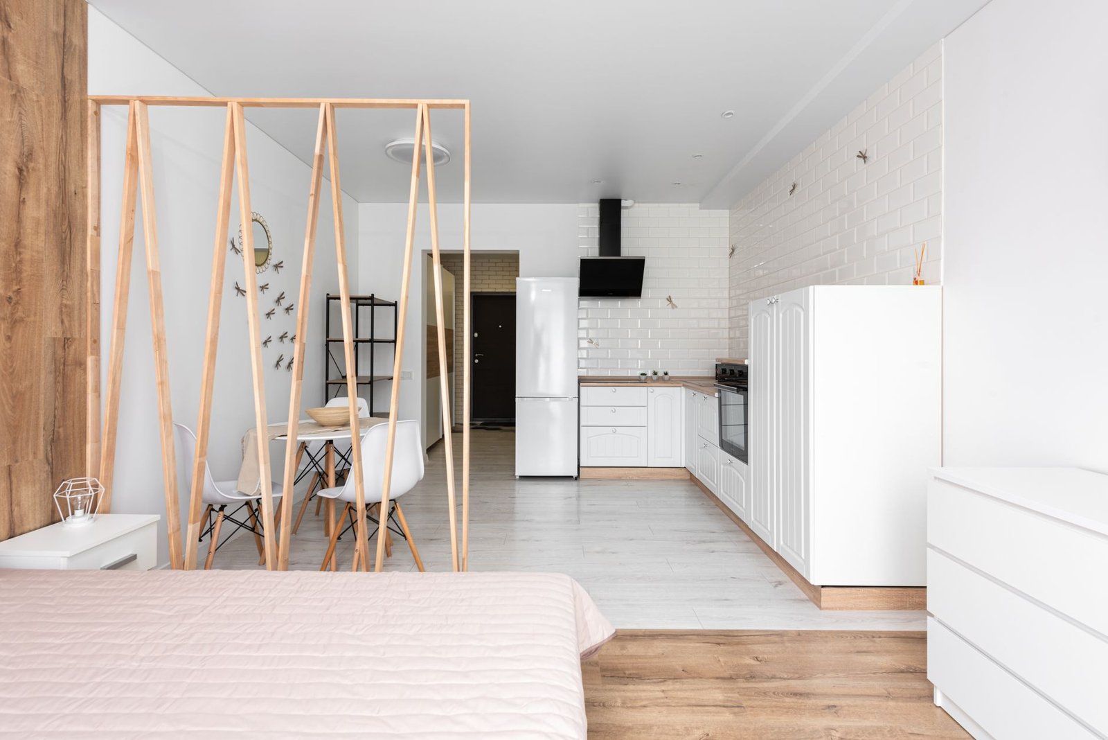 Bright studio apartment with distinct living and sleeping zones separated by a bookshelf divider and warm neutral decor
