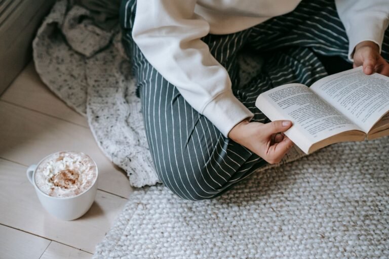 Warm reading corner with armchair, floor lamp, and chunky knit throw blanket near window with natural light