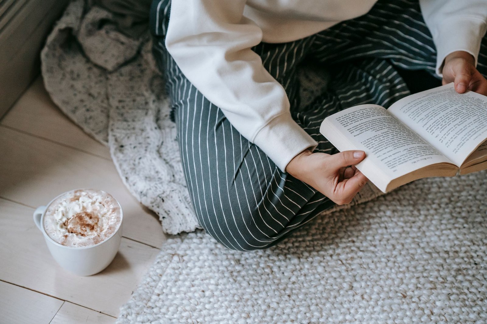 Warm reading corner with armchair, floor lamp, and chunky knit throw blanket near window with natural light