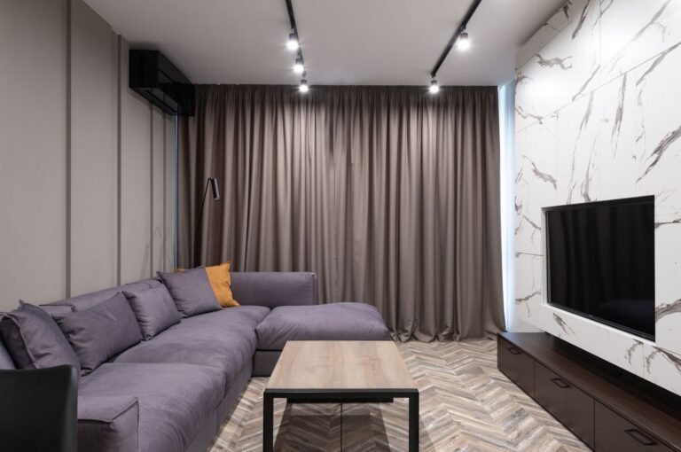 Warm rented flat living room with layered textiles, floor lamp, and freestanding bookshelf creating cozy atmosphere